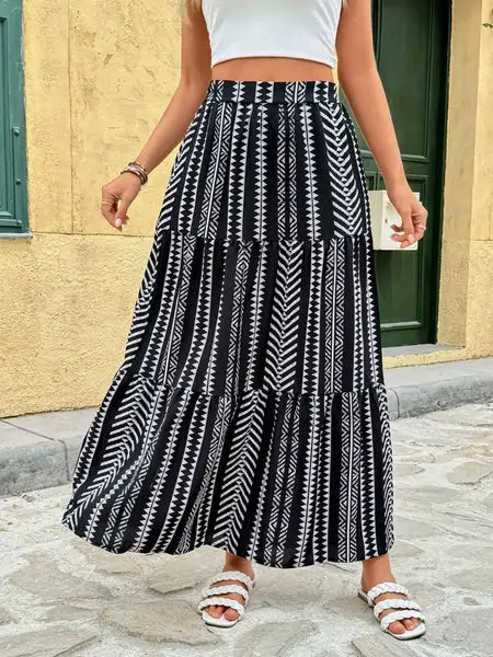 Close-up of a flowing ethnic-patterned black and white maxi skirt with white braided sandals, captured mid-movement.