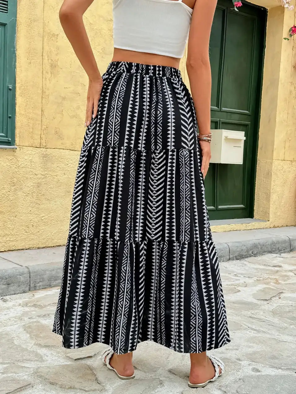 Back view of a black and white tribal print maxi skirt with tiered design, styled with a white crop top and flat sandals.
