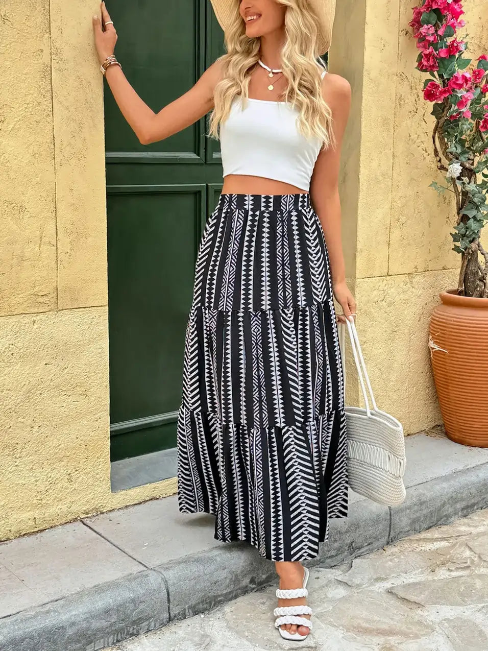 Smiling woman in a tribal print tiered black and white maxi skirt, styled with a white crop top and straw hat on a sunny street.